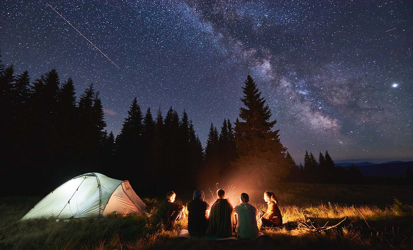 A group of campers around a campfire under a starry night sky
