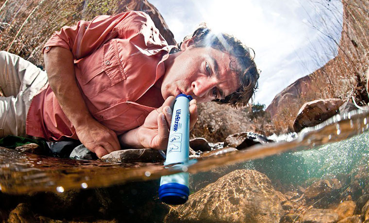 Man drinking water from a stream through a LifeStraw