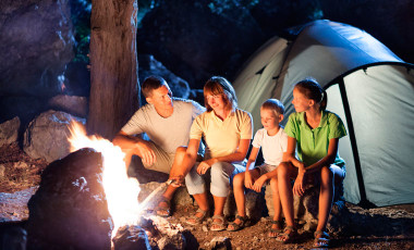 Family sitting by a campfire next to a tent