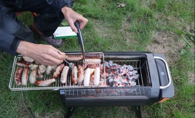 Man cooking sausages on the best camping grill