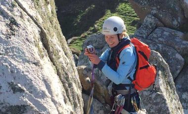 Female rock climber setting a cam carrying backpack