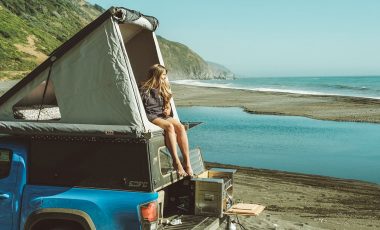 Woman in rooftop tent by the ocean