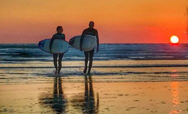 Couple walking with surfboards at sunset