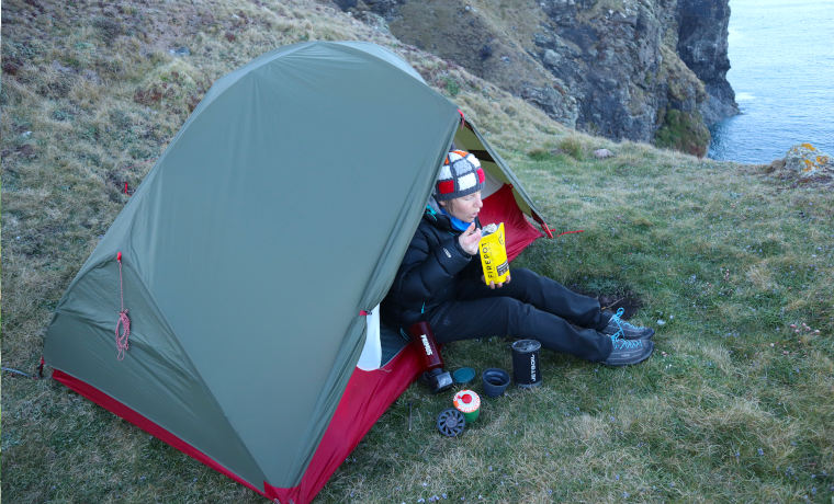 Woman eating backpacking food next to tent