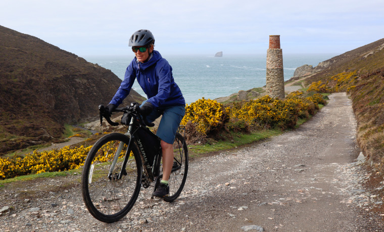 Woman cycling by the sea near mining chimney