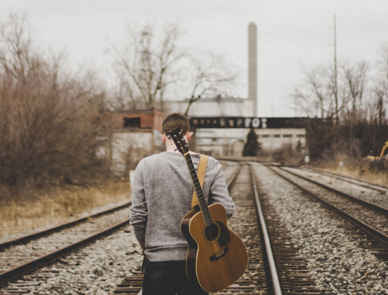 Man with guitar on railway tracks